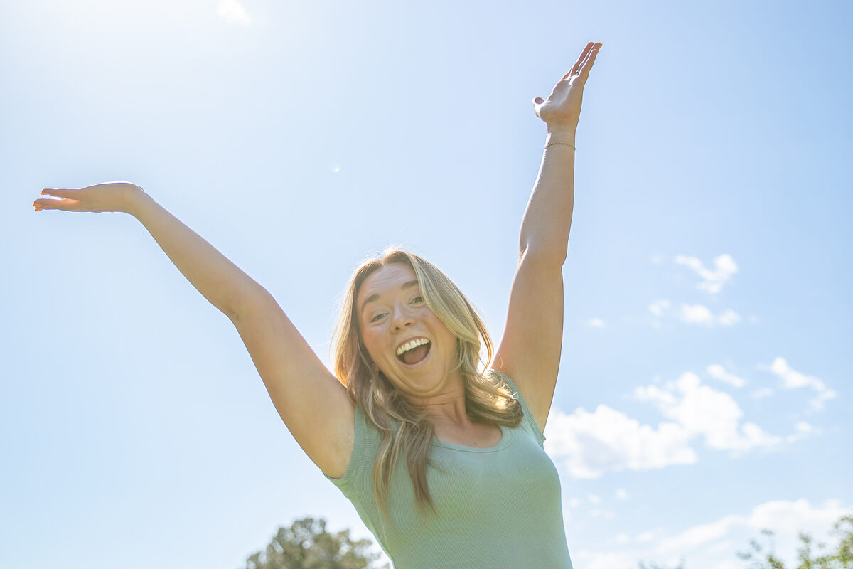 Autumn Flowers with her arms in the air under a blue sky